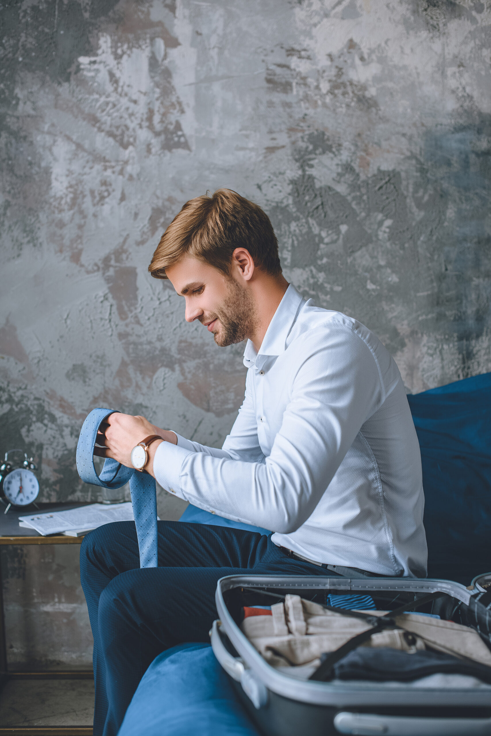 smiling businessman packing luggage in suitcase in bedroom at home